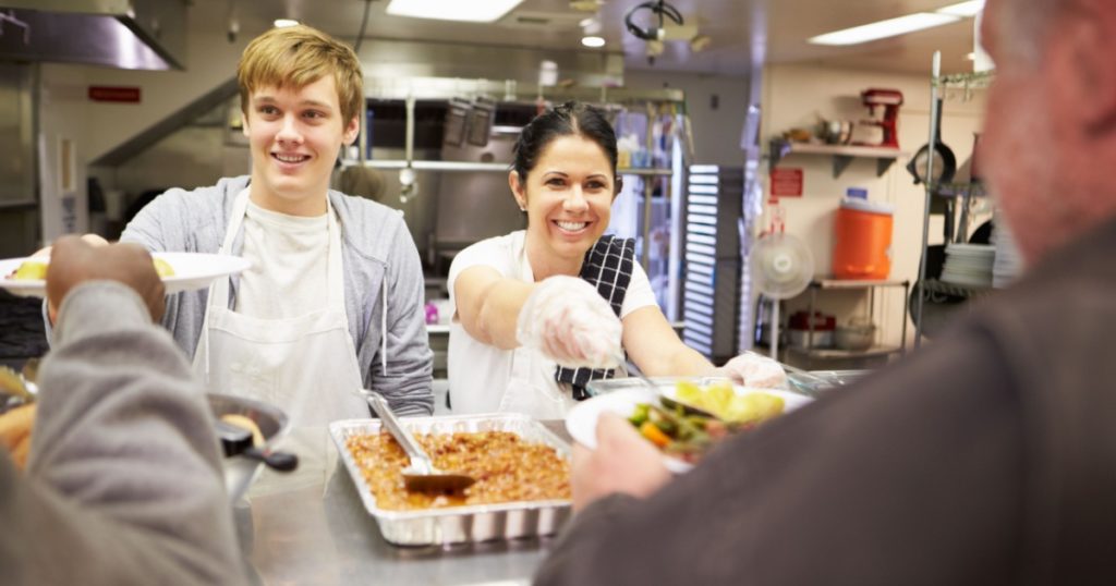 Staff Serving Food In Homeless Shelter Kitchen