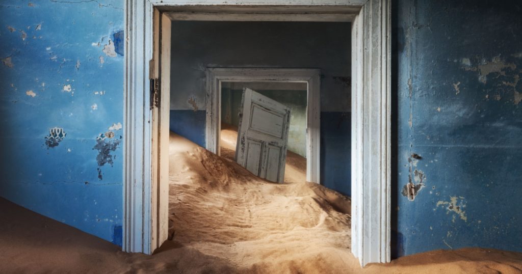 Abandoned building and the door being taken over by encroaching sand, Kolmanskop ghost town, Namib Desert