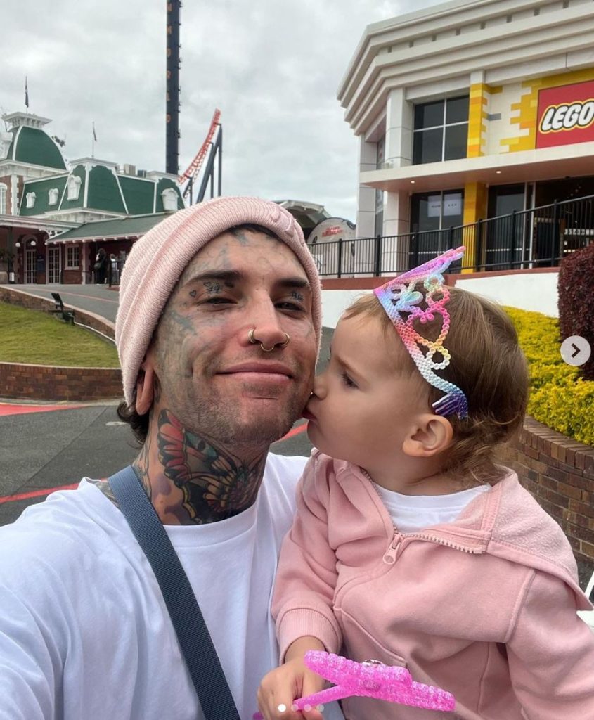 Little girl wearing a grown gives her dad a kiss on the cheek. Theme Park in the background. 