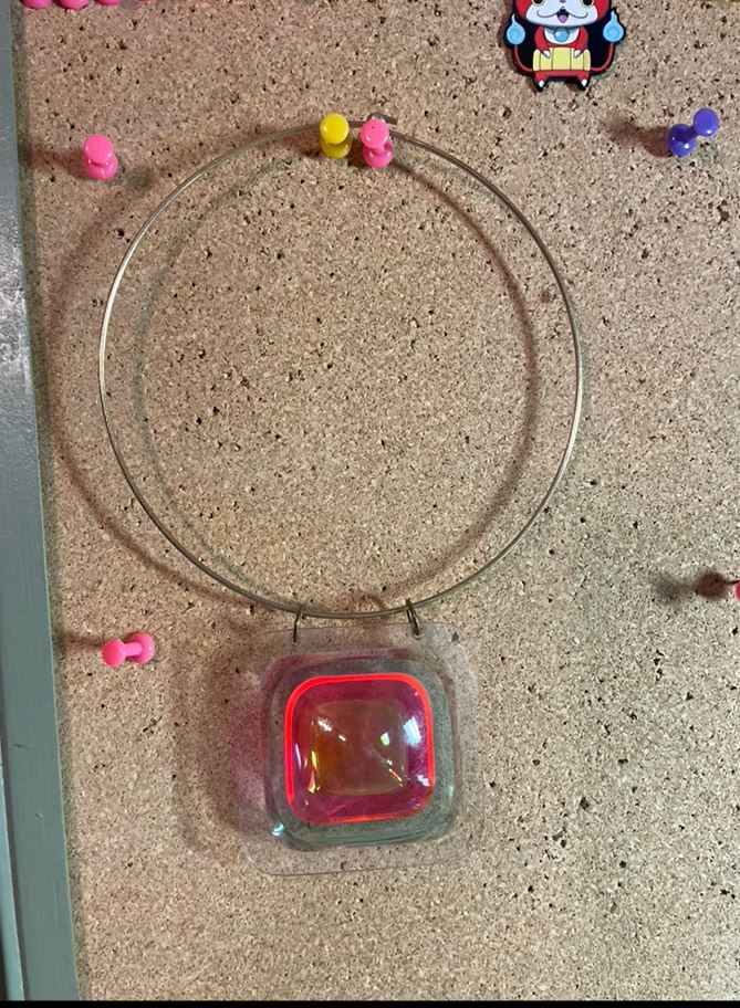 A necklace pinned on a corkboard with thumbtacks in the background. 
