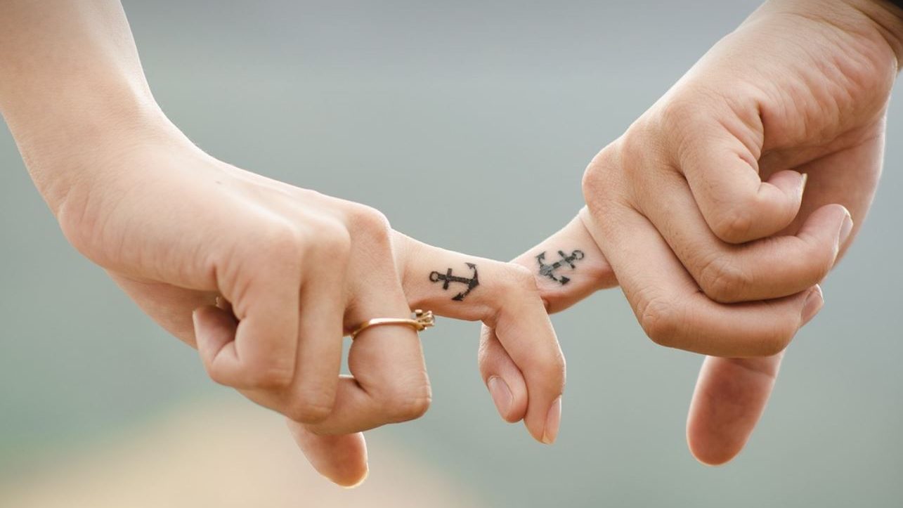 Man's and woman's hand laced by index fingers with matching tattoos. 