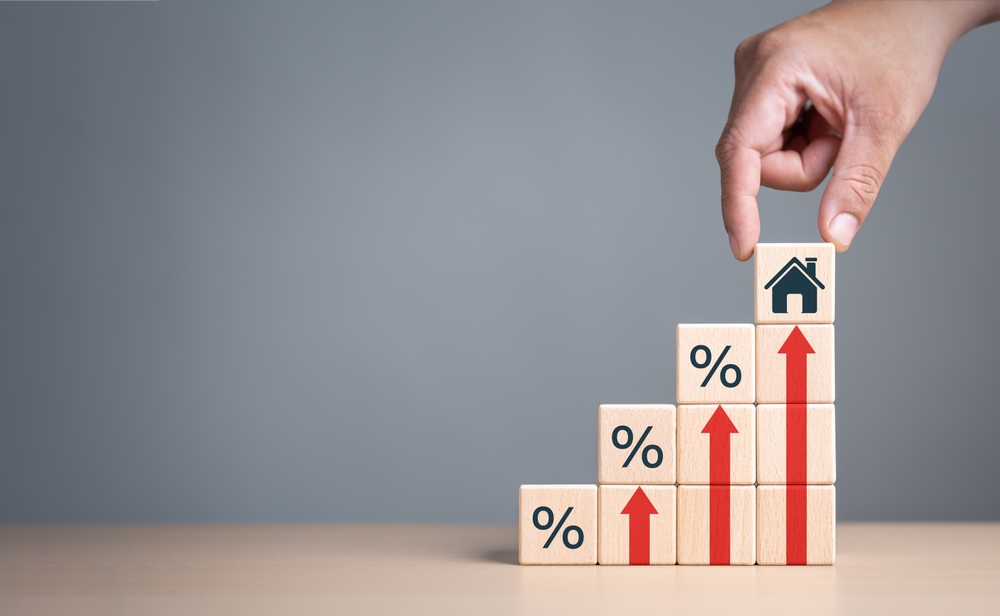 Real estate property investment concept. Asset management, Interest rates, inflation, loan mortgage, increase tax. Hand holding house icon on wooden cube from stack block with percent and rise arrow.

