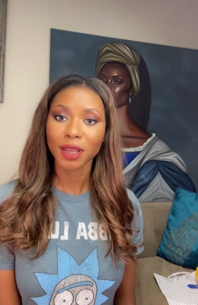 A woman speaking in front of a large portrait. 