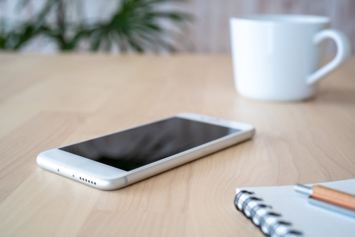 A smartphone, notebook, pen, and cup on the table.
