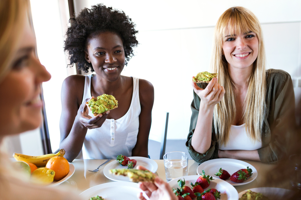 Shot of group of friends laughing while eating healthy food at home.