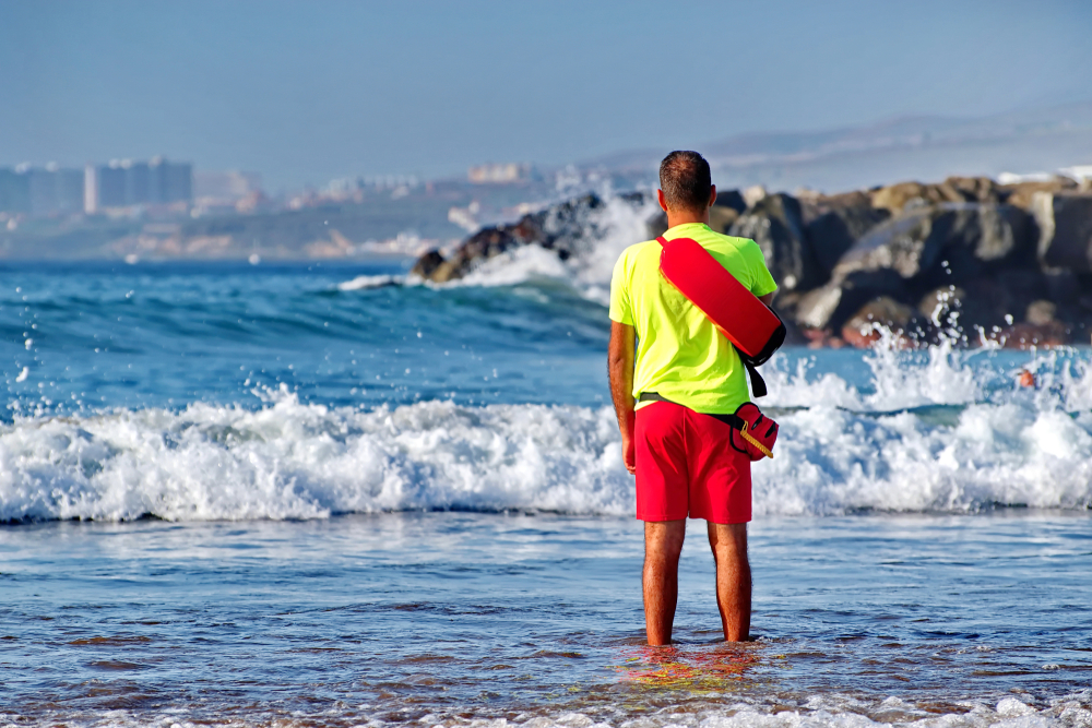 Male in beach lifeguard uniform stands in the water and oversees order and the safety