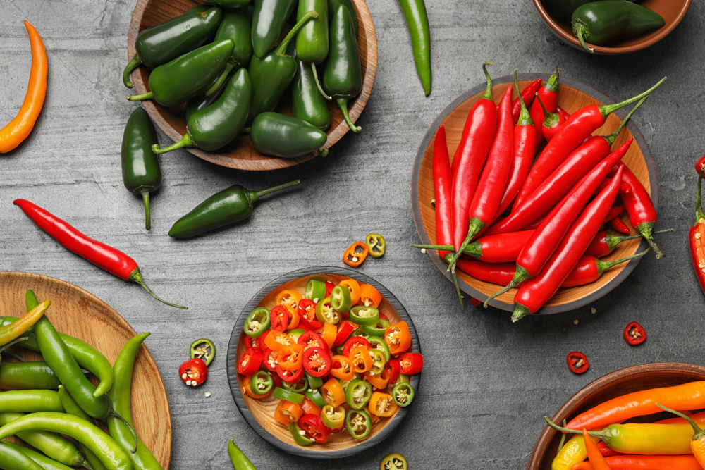 Different ripe hot chili peppers on grey table, flat lay