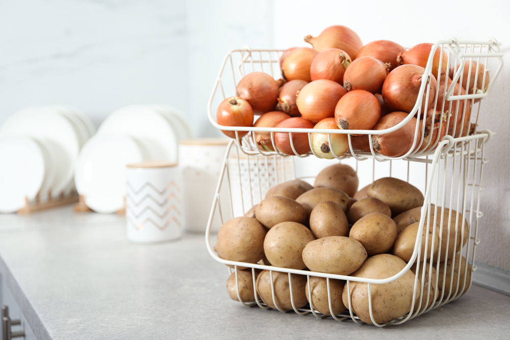 Container with potatoes and onions on grey kitchen counter, space for text. Orderly storage