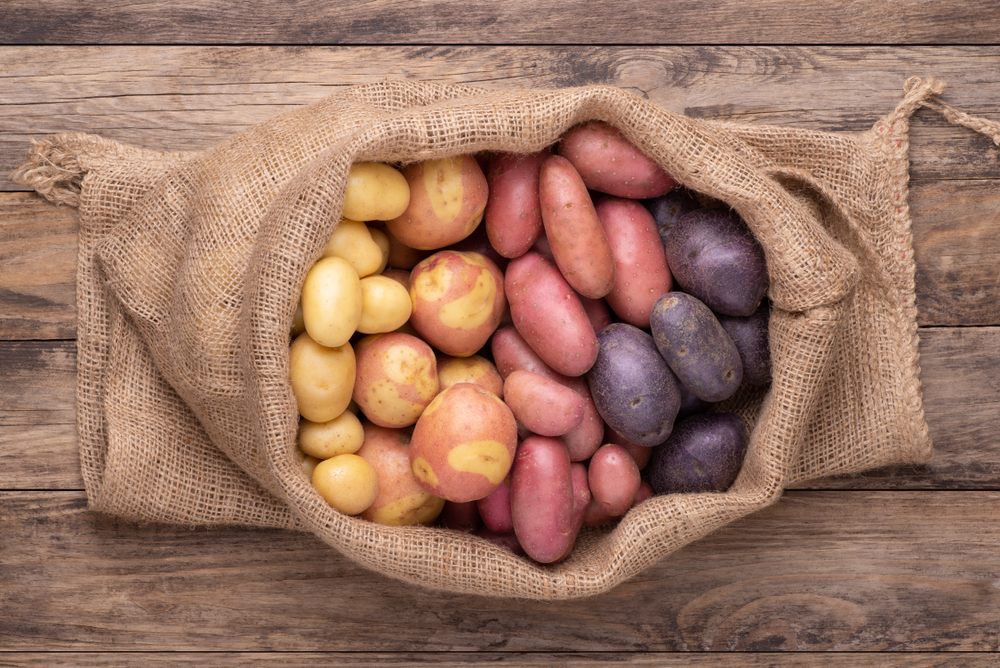 Different types of potatoes in a sack on wooden rustic table