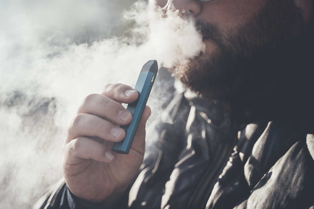 Man smokes new Vape Pod System, inhales and exhales vapor of electronic cigarette, vaping concept, selective focus, toned