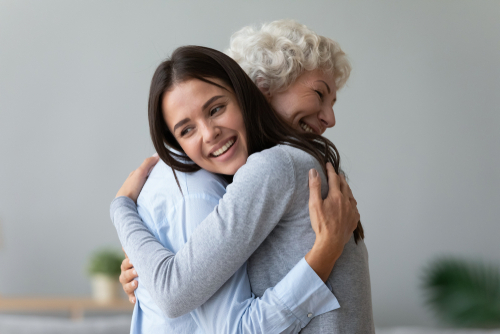 Happy young lady adult daughter granddaughter visiting embracing hugging old senior retired grandmother cuddling bonding, two age generations women expressing love and care at reunion meeting at home
