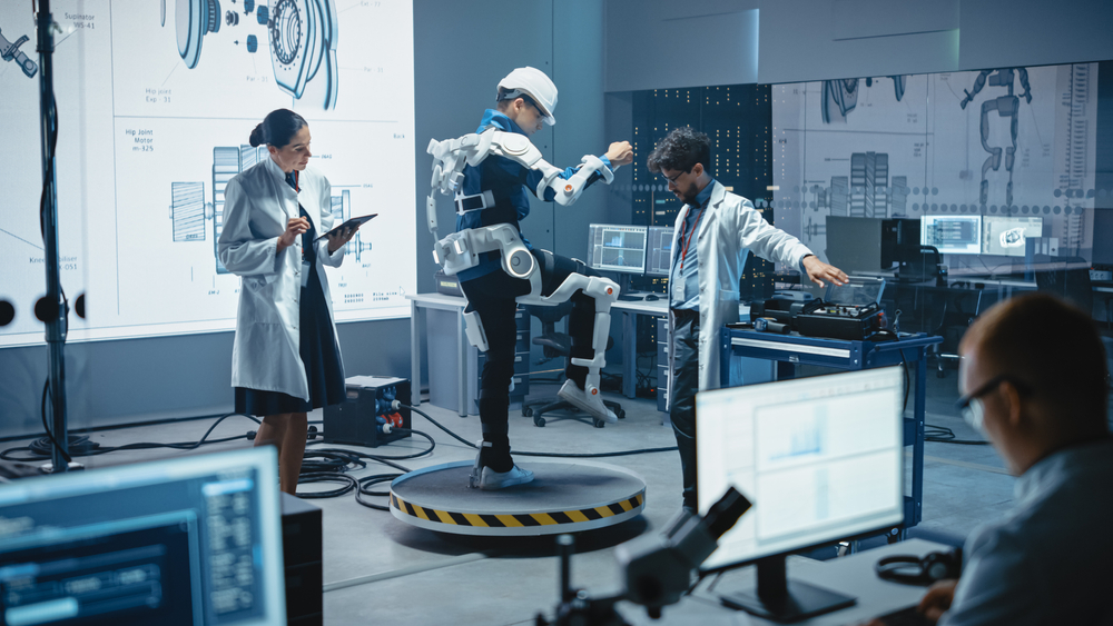 In Robotics Development Laboratory: Engineers and Scientists Work on a Bionics Exoskeleton Prototype with Person Testing it. Designing Wearable Exosuit to Help Disabled People, Warehouse Workers
