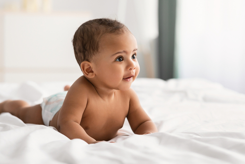 Curious adorable little African American infant lying on bed
