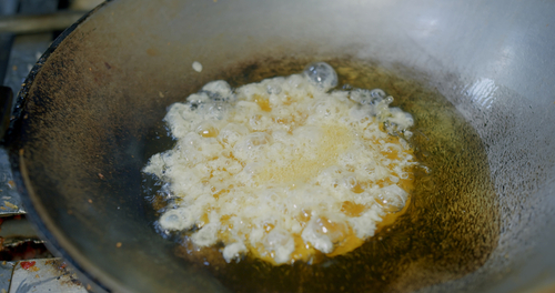 Close up chef cooking Thai style food deep fried omelet egg in hot oil pan at the kitchen, simple street food in Thailand