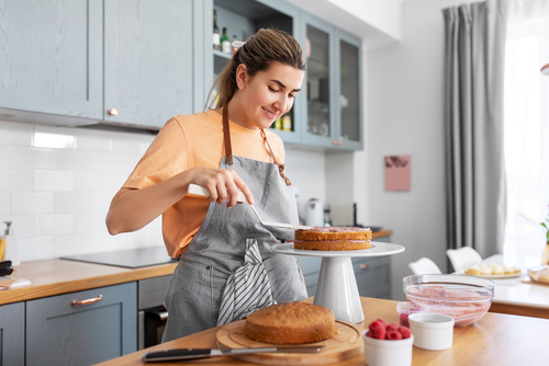 culinary, baking and cooking food concept - happy smiling young woman making layer cake on kitchen at home