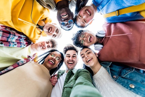 Multiracial group of young people standing in circle smiling at camera - International teamwork students hugging together - Human resources and youth culture concept