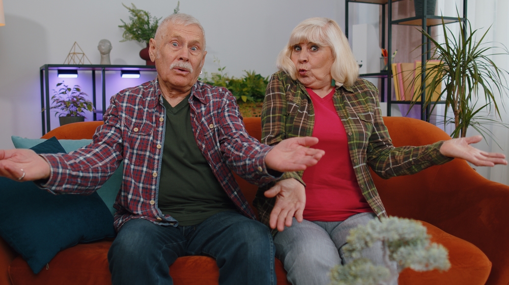 Senior family grandparents man woman raising hands in indignant expression, asking why, what reason of failure, demonstrating disbelief irritation by troubles. Mature grandmother grandfather at home