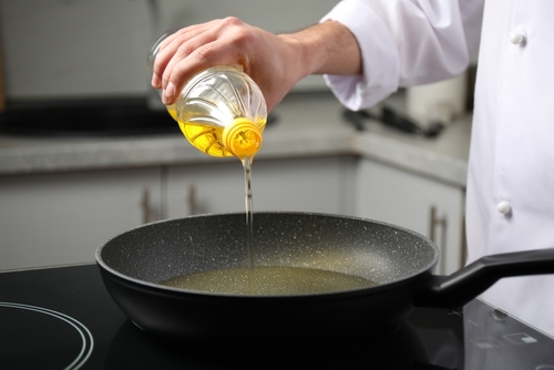 Man pouring cooking oil from bottle into frying pan, closeup
