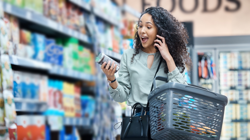 Supermarket, grocery shopping and surprise of a black woman on a phone call at a retail store. Wow, happy and omg facial expression of a customer hearing deal, price sale on stock and discount food
