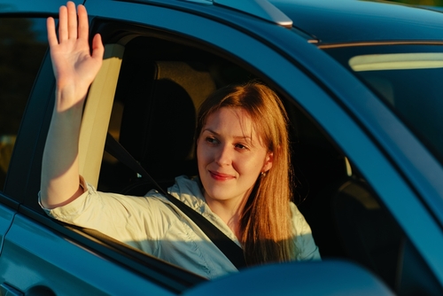 Happy young woman waving hand from car window