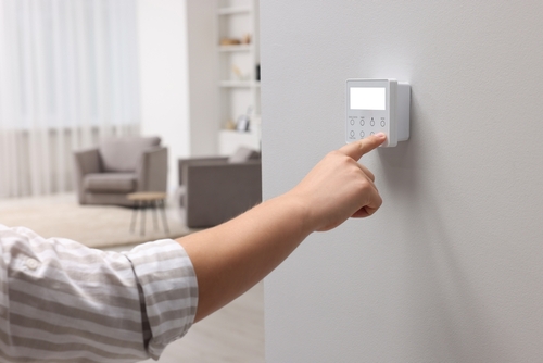 Man adjusting thermostat on white wall indoors, closeup. Smart home system