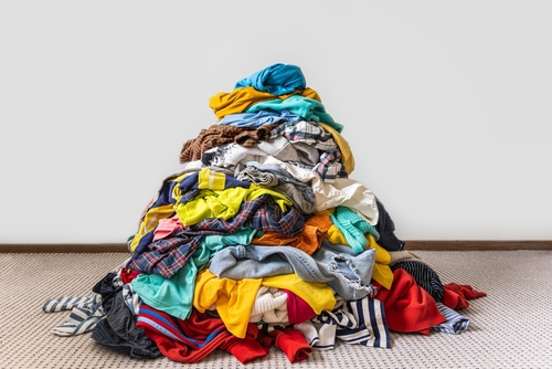 Pile of unfolded dirty clothes for laundry on the chair. Heap of used clothes for donation and recycling. Concept of minimalism, mess and wardrobe cleaning