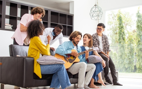 Group of diverse friends or people wearing casual clothes, relax smiling with happiness, party celebration, sitting in living room at cozy home, playing guitar and singing. Birthday, New Year Concept