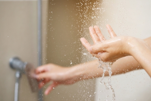 A woman uses hand to measure the water temperature from a water heater before taking a shower