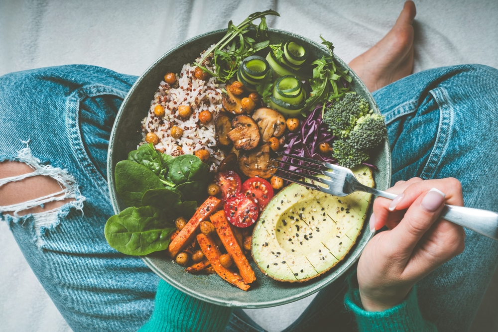 Woman eating healthy meal. Bowl with rice, quinoa, avocado, cucumber, broccoli and cucumber. Healthy diet, lunch or dinner. Healthy food plate