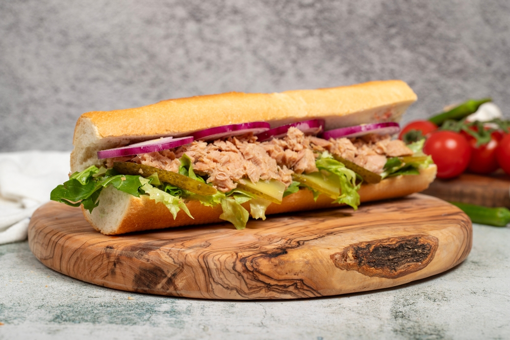 Tuna sandwich on wood serving board. Sandwich made with tuna meat, special sauce, purple onion, pickles and greens