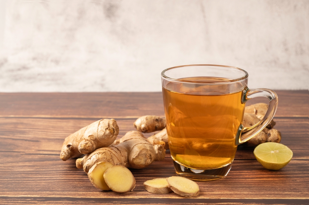 Hot ginger tea with ginger and lime on wooden table.