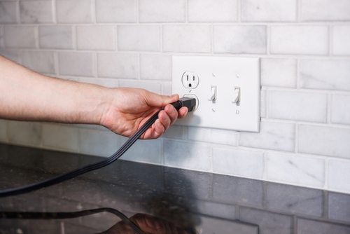 Hand Turning Off Light Switch with Electrical Outlet in Background