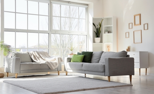 Interior of light living room with cozy grey sofas near big window
