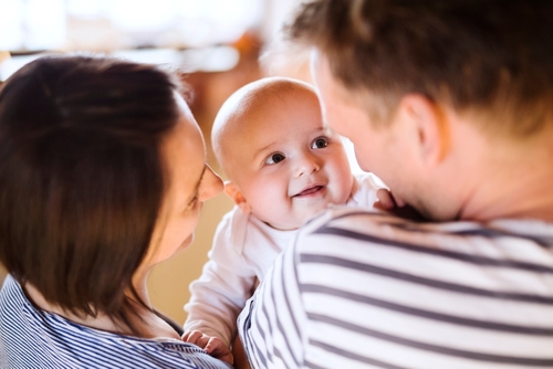 Happy parents holding and playing, kissing small baby, carrying him around house. Unconditional paternal love, family moment.

