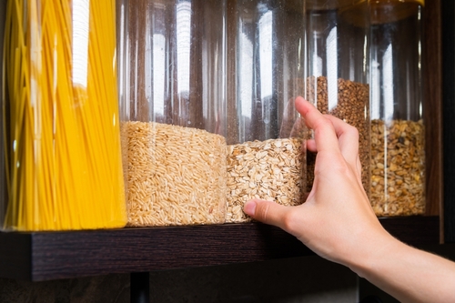 Food storage, wooden shelf in pantry with grain products in storage jars. Woman taking food for cooking