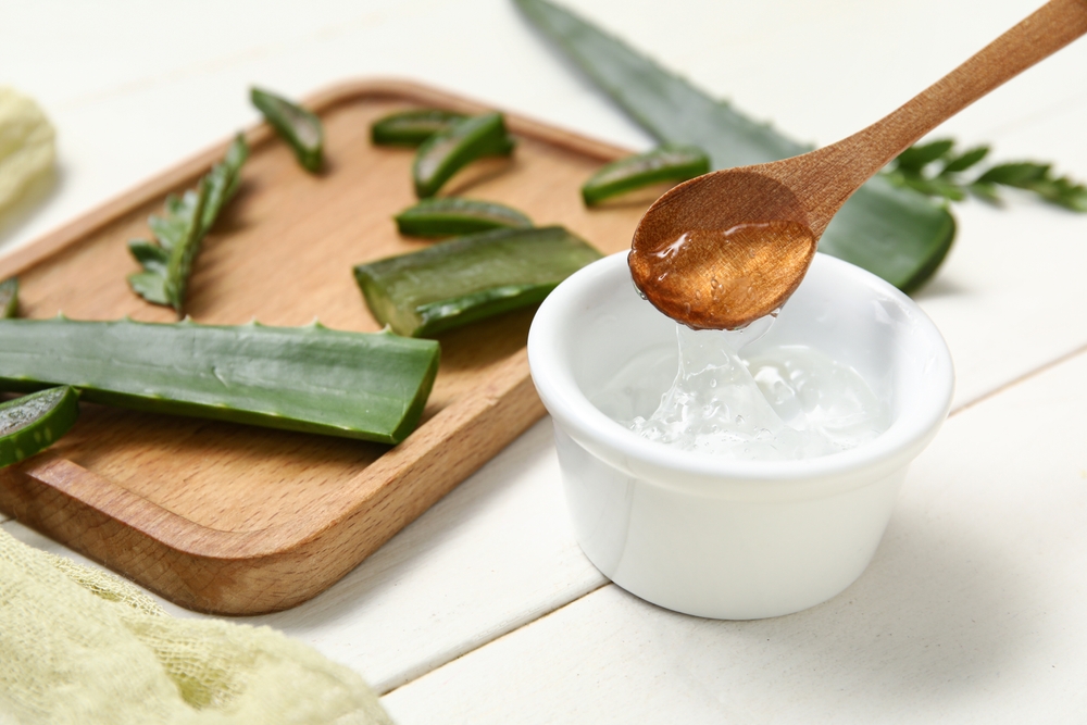 Bowl of aloe vera gel and board with leaves on white wooden background