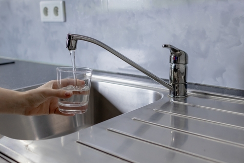 Water is running from the tap in the kitchen. A girl takes water into a glass from the tap in the kitchen