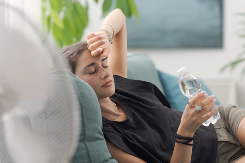 Exhausted young woman at home during the summer heatwave, she is resting on the couch and holding a water bottle