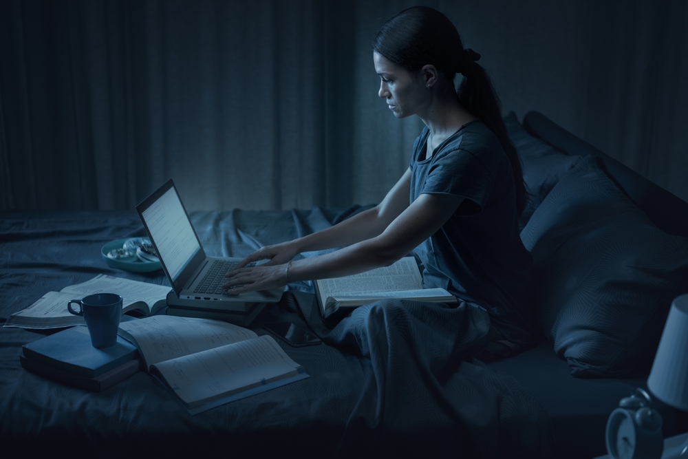 Focused female student sitting in bed and typing on her laptop, she is pulling an all-nighter and studying before the exam