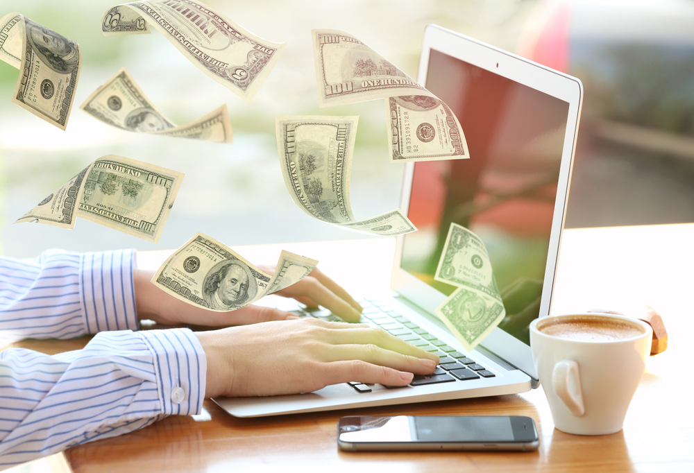 Money flying out of laptop while woman using it at table in office