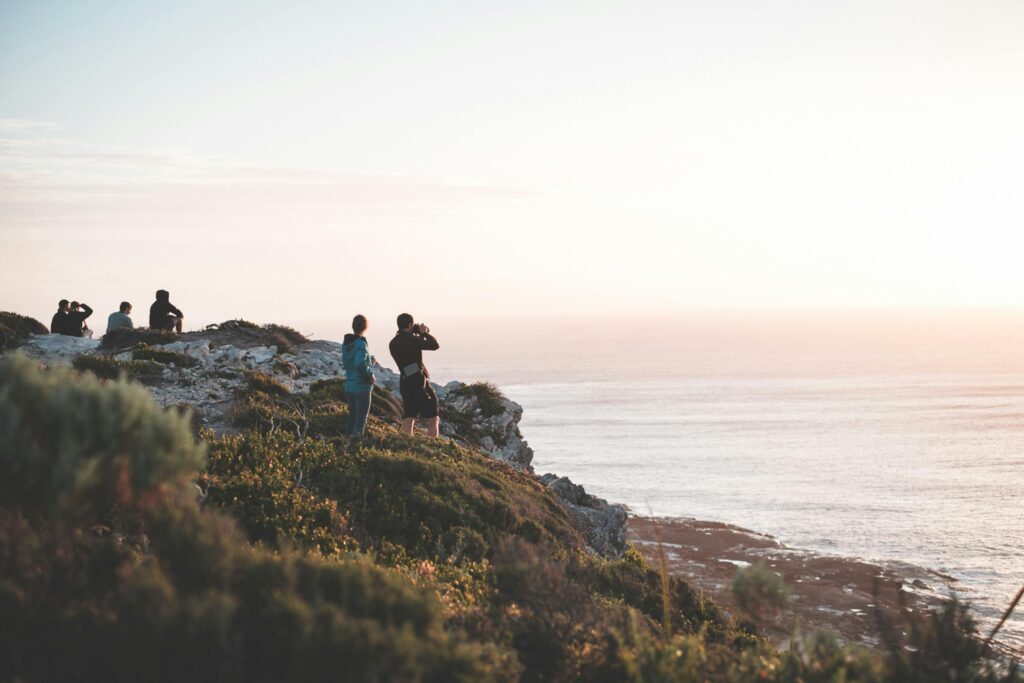 Group of travelers resting on rocky seashore at sunset