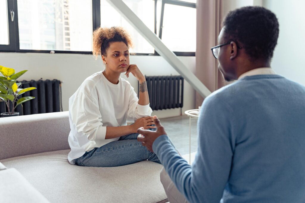 woman with white shirt talking to man on couch 