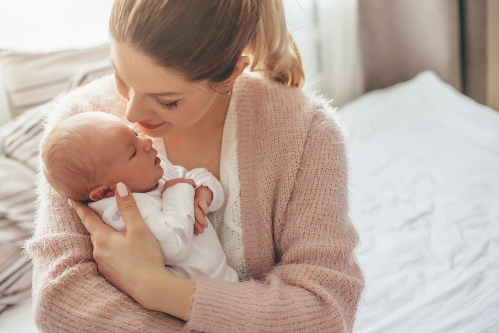Home portrait of a newborn baby with mother on the bed. Mom holding and kissing her child.