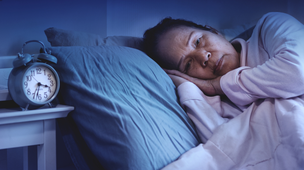 60s or 70s Asian senior woman having sleep disorder, sitting in bed look sad.Lonely grandmother have Difficulty falling asleep. Waking up often during the night and having trouble going back to sleep.