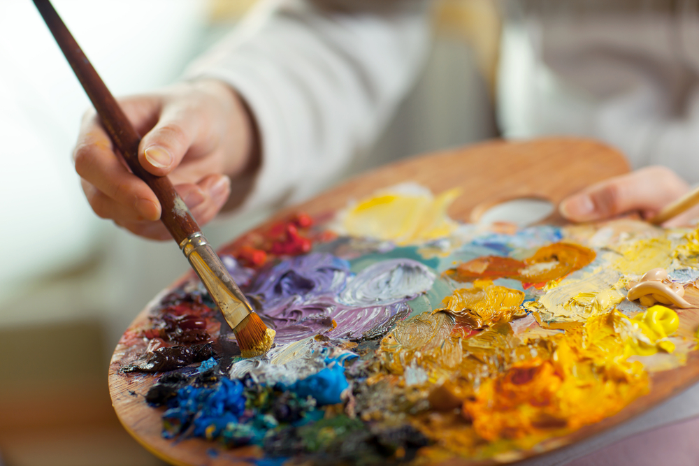 artist brush mix color oil painting on palette is holding in his hand closeup