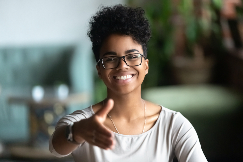 Happy african American young woman in glasses stretch hand for handshake greeting introducing to someone, smiling black biracial millennial female hr agent in spectacles get acquainted at meeting
