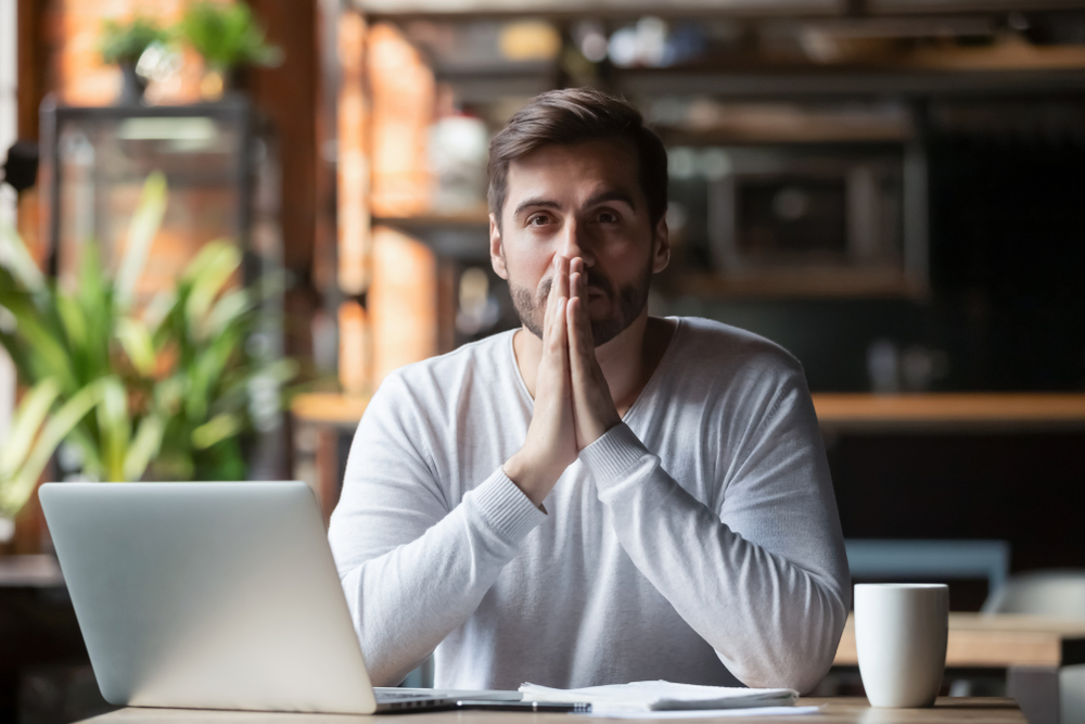 Thoughtful doubtful businessman in tension thinking make difficult decision at work, stressed man put hands in prayer pray with hope pondering reflecting concerned about problem challenge sit at desk