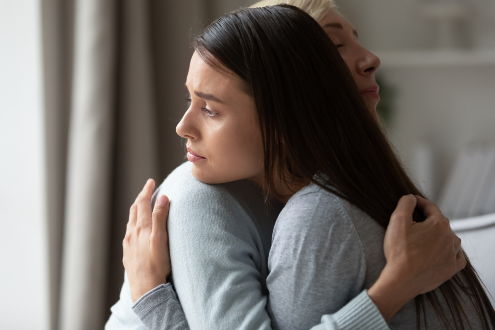 Side view caring middle aged woman embracing comforting soothing sad millennial daughter, demonstrating support and love. Upset worried young lady cuddling hugging empathic loving older mother.
