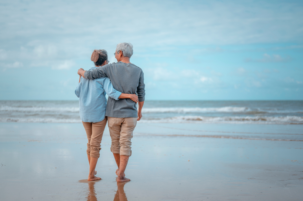 Senior couples walking on the beach at sunny day, plan life insurance with the concept of happy retirement.