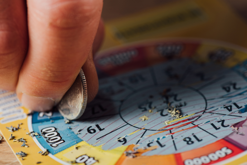 cropped view of gambler scratching lottery ticket with silver coin